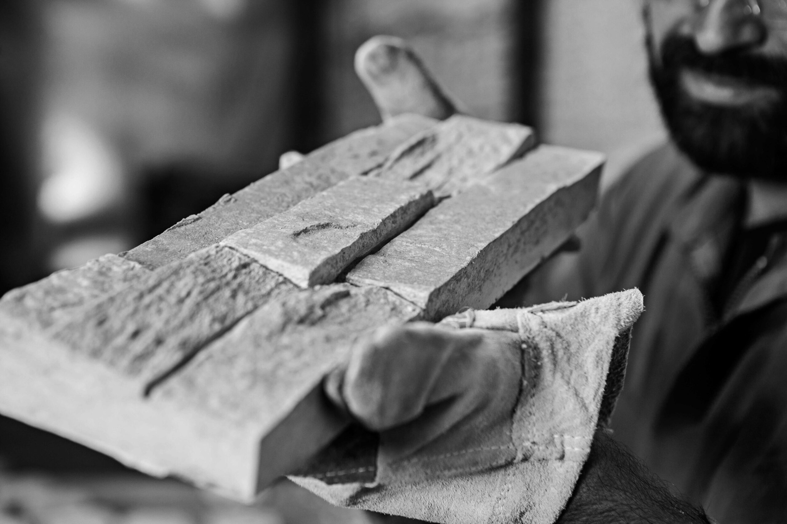 Primer plano en blanco y negro de las manos de un operario usando guantes de protección, sosteniendo con cuidado una pieza de revestimiento recién desmoldada con textura de piedra natural.