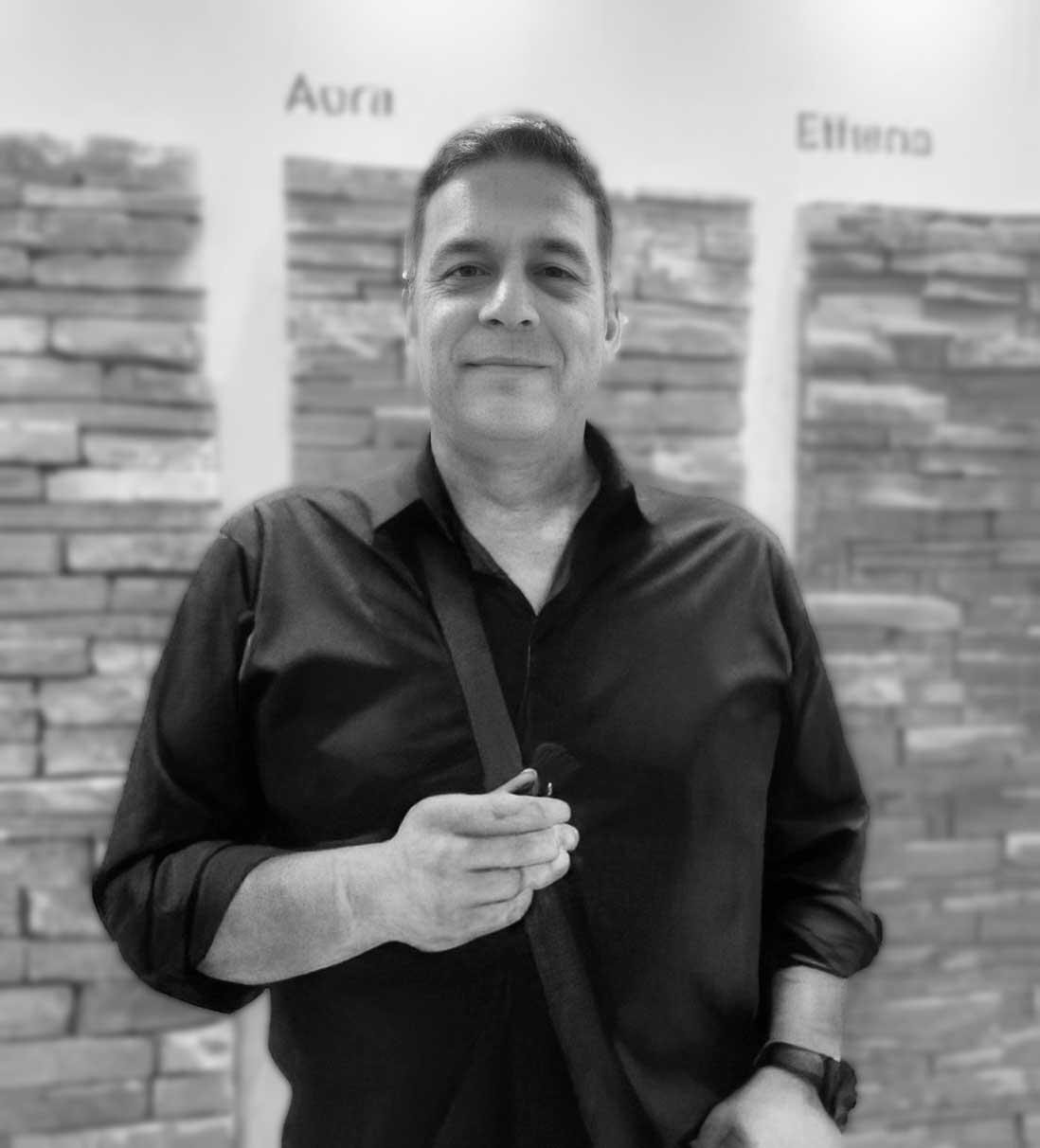 Retrato en blanco y negro de un emprendedor del Programa Génesis posando frente a muestras de revestimientos, representando el éxito en la fabricación propia de piezas.