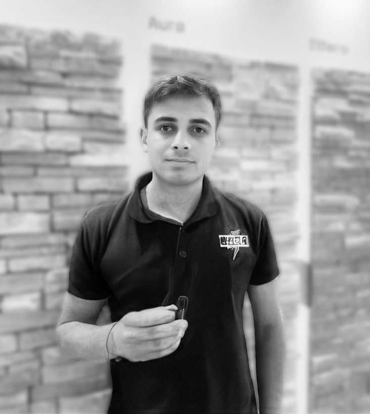Retrato en blanco y negro de un emprendedor del Programa Génesis posando frente a muestras de revestimientos, representando el éxito en la fabricación propia de piezas.